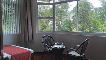 A room with a bed, two wicker chairs, a small table, and a TV.