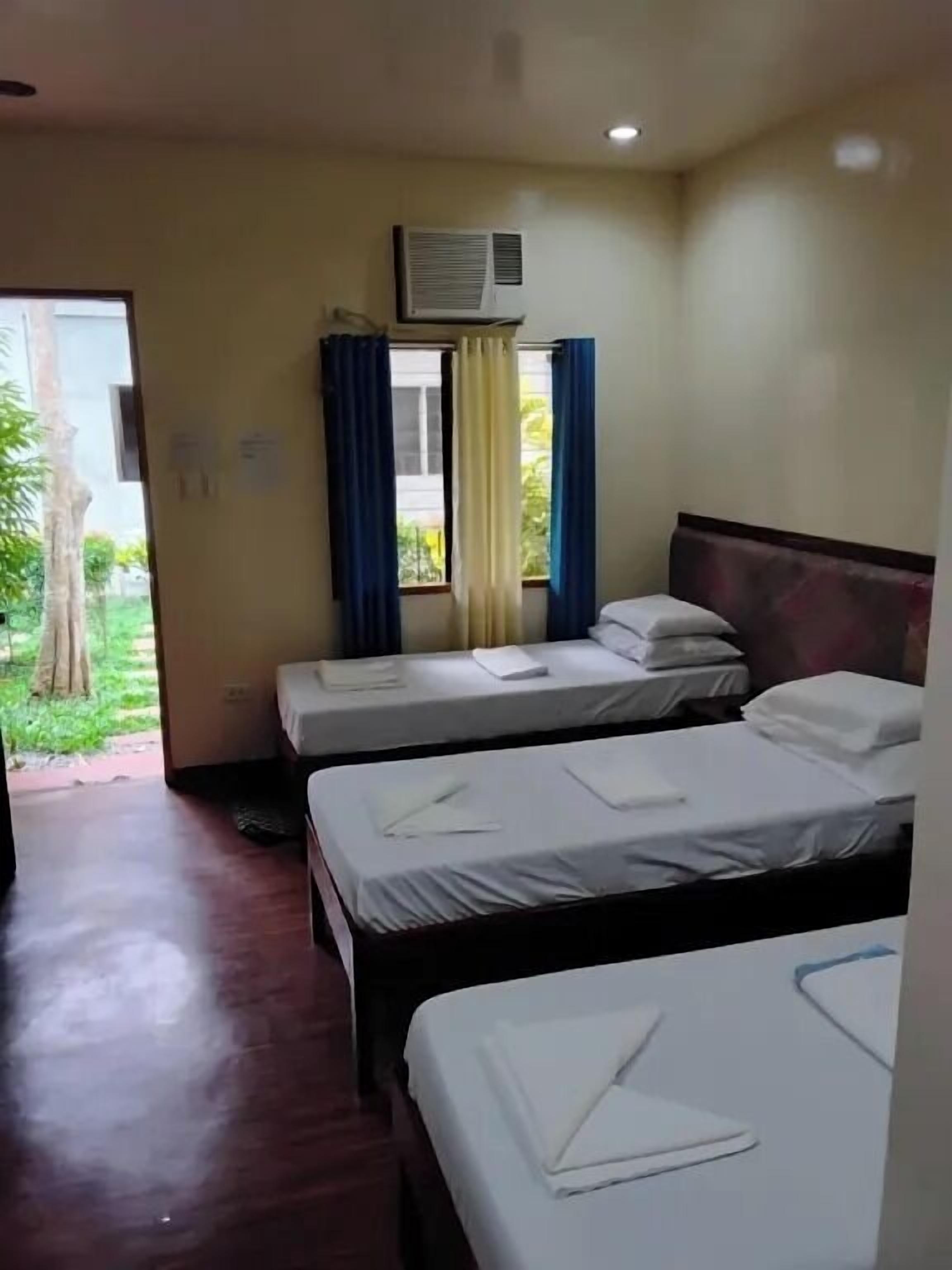 Habitación de hotel con dos camas, una ventana con cortinas, un equipo de aire acondicionado y vista a zonas verdes.