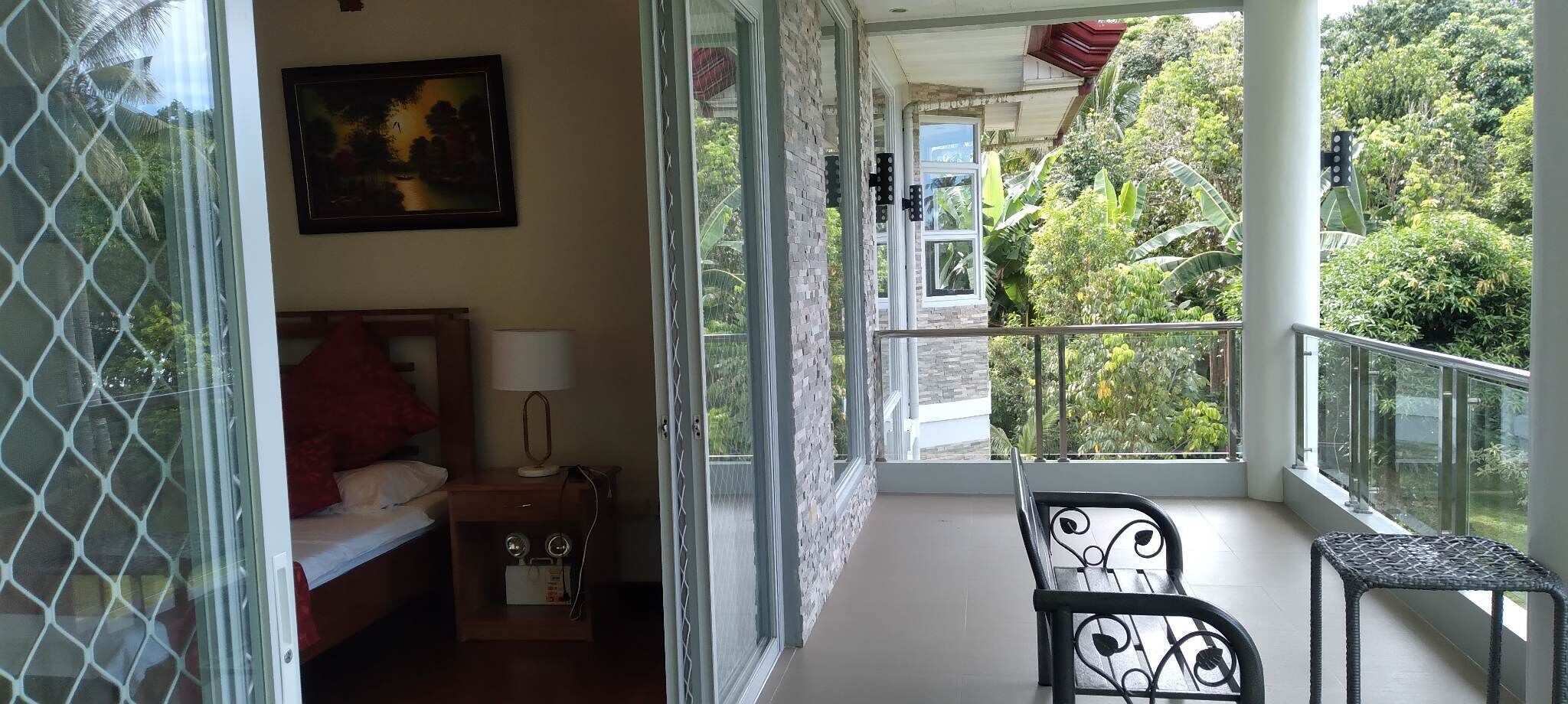 A balcony with a bed, a nightstand, a lamp, and a chair.