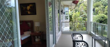 A balcony with a bed, a nightstand, a lamp, and a chair.