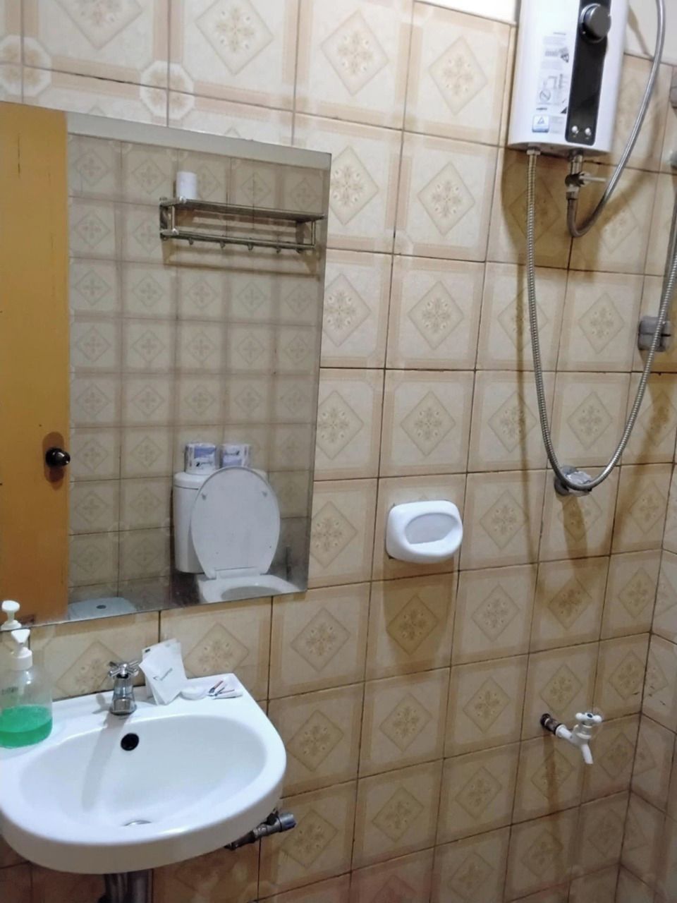 A bathroom with a toilet, sink, mirror, shower, and a soap dispenser.