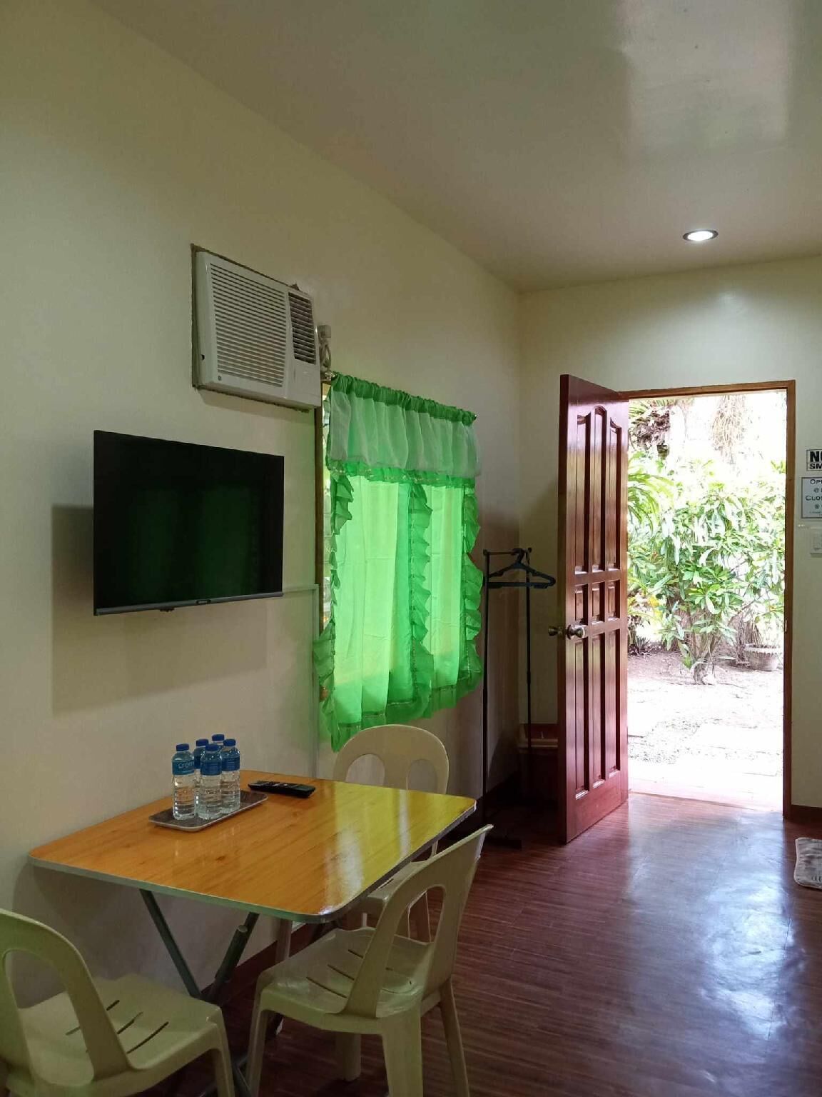 A room with a wooden table, two chairs, a television, and a window with green curtains.