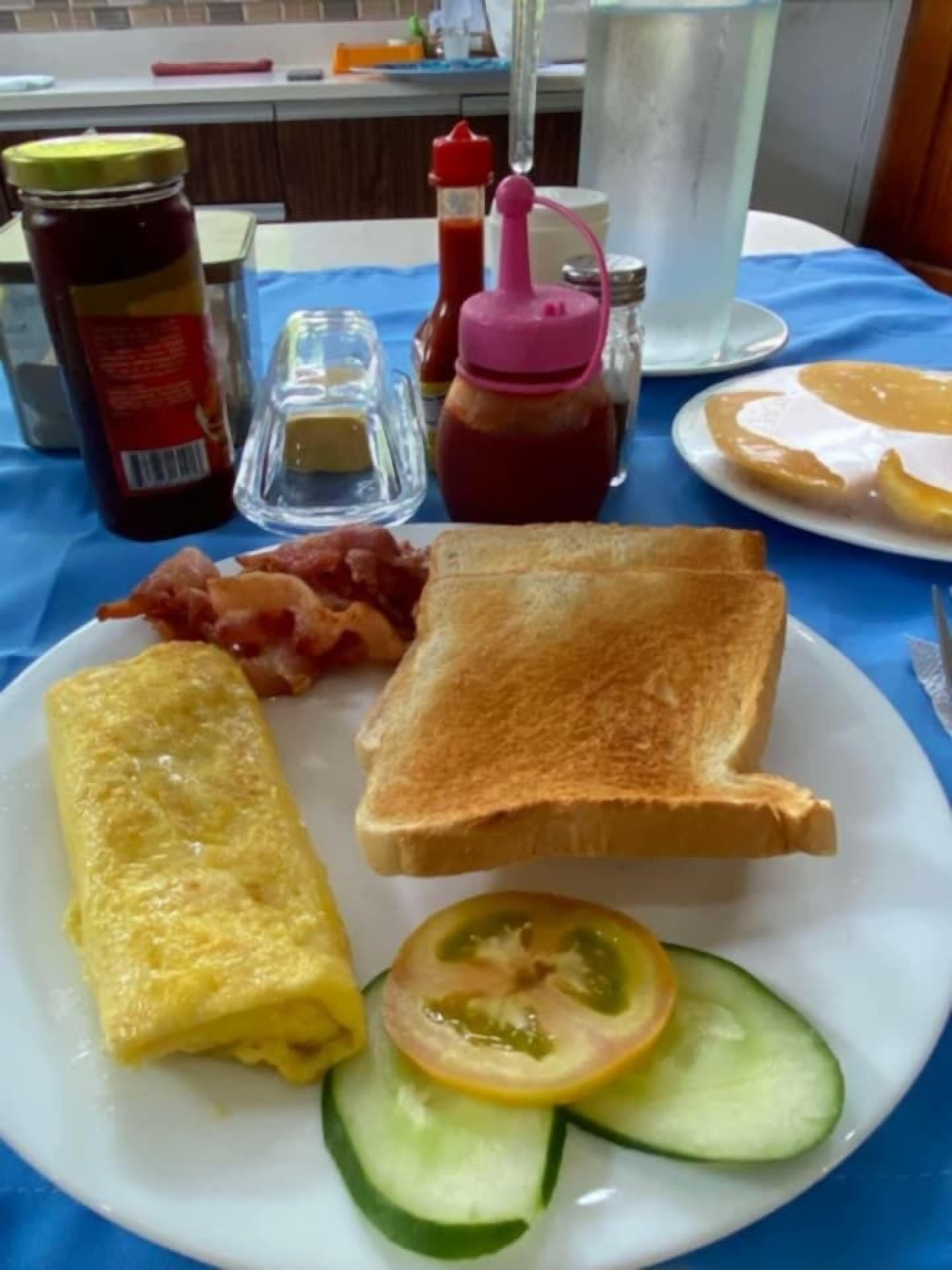 Une assiette de petit-déjeuner comprenant des toasts, du bacon, une omelette et des tranches de concombre.