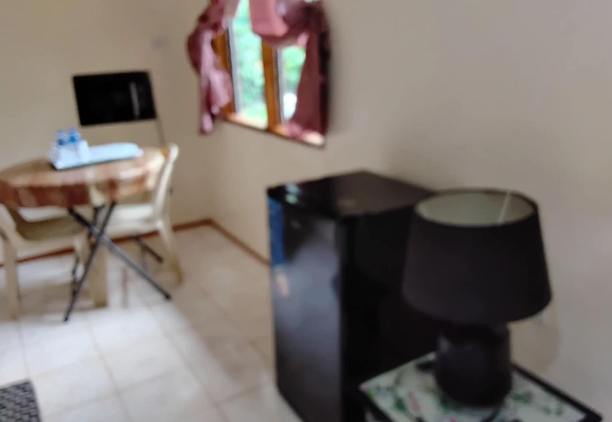 Una habitación con un escritorio, una silla, un armario negro y una lámpara sobre una mesita.