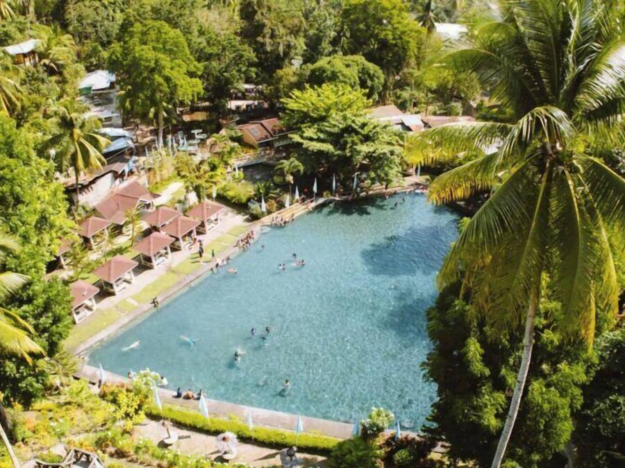 An aerial view of a resort with a large swimming pool surrounded by lush greenery and palm trees.