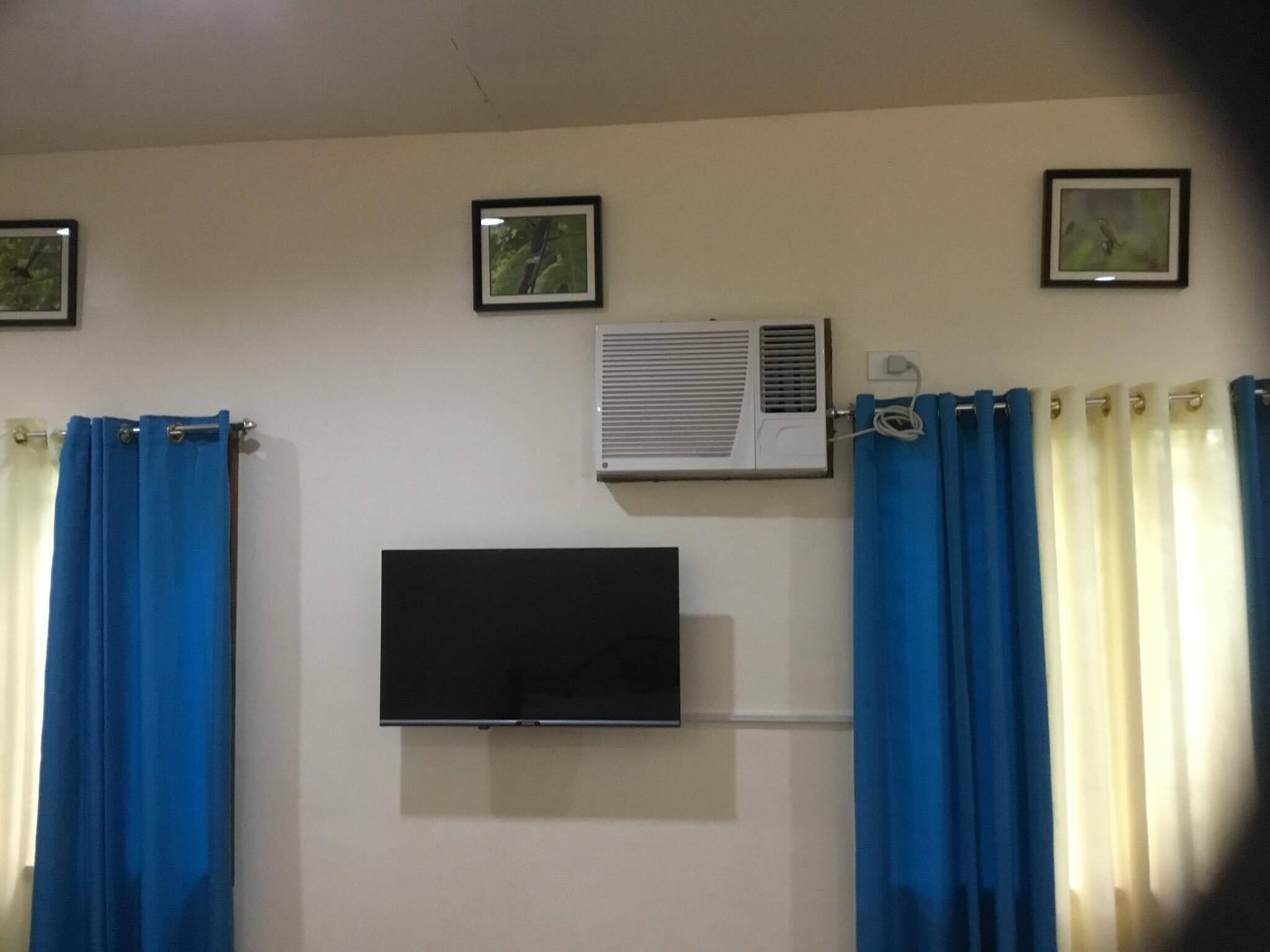 Une pièce équipée d’un téléviseur fixé au mur, d’un appareil de climatisation et de deux tableaux encadrés.