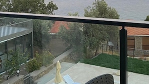 A balcony with a view of the sea, lounge chairs, and a glass building. - Assos Luna Houses (Ayvacik)