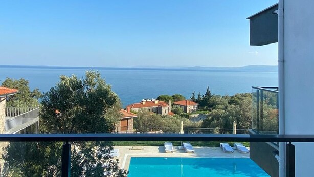A balcony with a clear view of a swimming pool and a distant body of water. - Assos Luna Houses (Ayvacik)