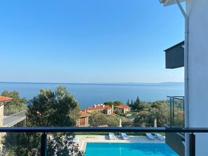 En balkon med frit udsyn til en swimmingpool og et fjerntliggende vandareal.