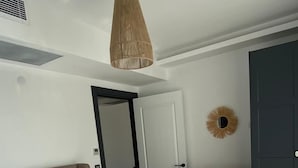A bedroom with a bed, a hanging light fixture, a door, and a small shelf. - Assos Luna Houses (Ayvacik)