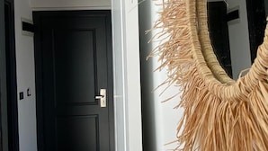 A hallway with a black door, a white wall, and a woven wall hanging. - Assos Luna Houses (Ayvacik)
