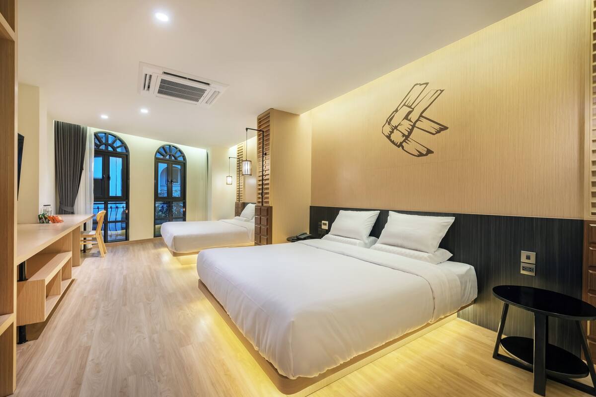 Une chambre d’hôtel moderne équipée de deux lits, d’un bureau et d’une chaise. Elle dispose de grandes fenêtres avec des rideaux, d’un climatiseur mural et d’une œuvre d’art originale accrochée au mur.