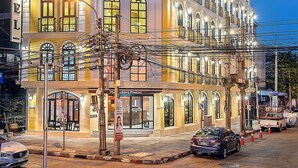 Un hotel de varios pisos con un reloj destacado en la fachada, varios balcones y una entrada bien iluminada.