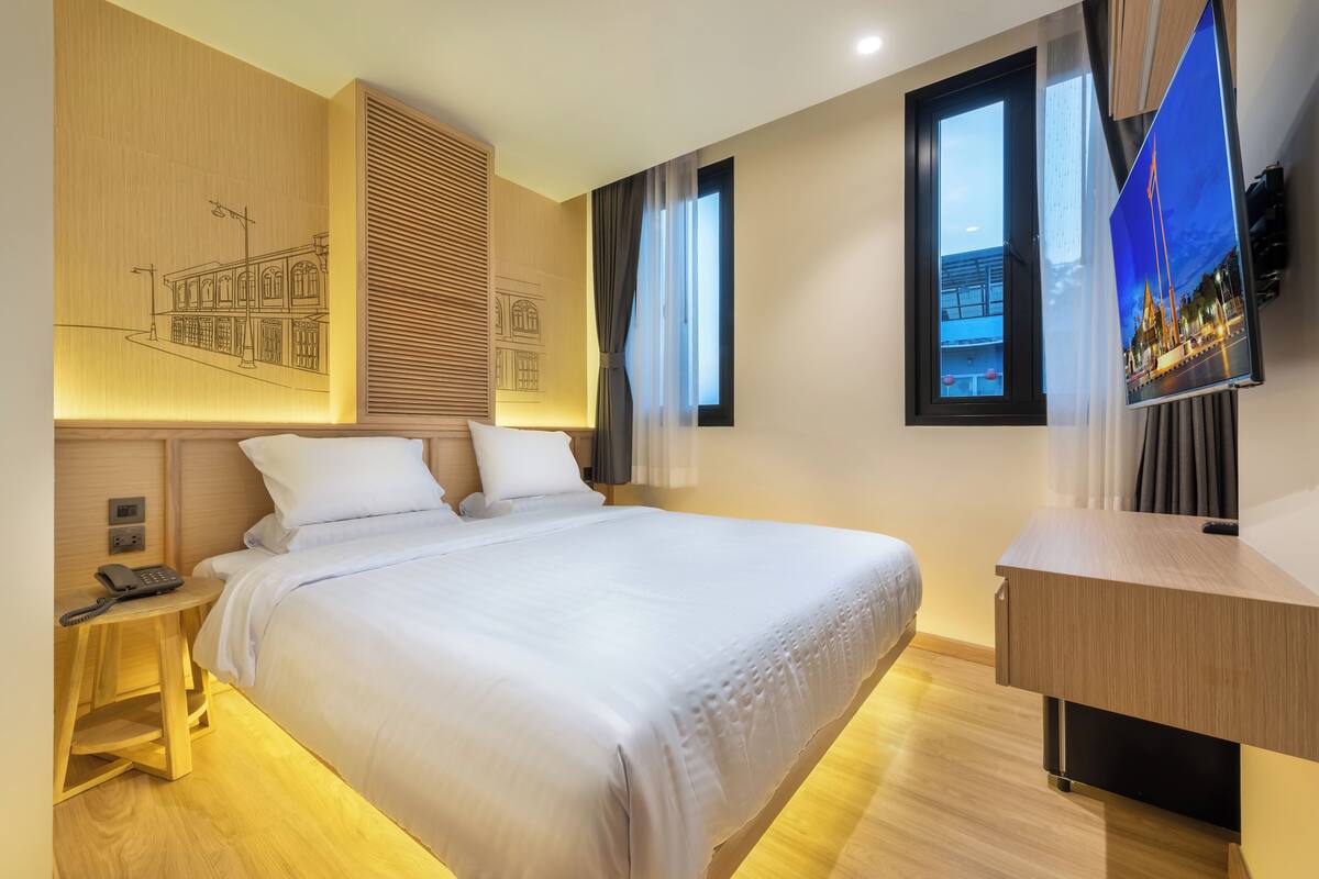 Une chambre d’hôtel avec un grand lit, une table de chevet en bois, un bureau et un téléviseur fixé au mur.