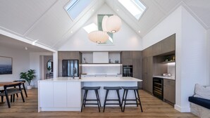 A modern kitchen with a central island, bar stools, and pendant lighting. - Marjon Peak Retreat | Spa, Pool & Mountain Views (Wānaka)