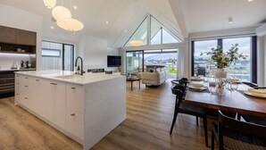 A spacious kitchen with a large island, modern pendant lights, and a view of the outdoors. - Marjon Peak Retreat | Spa, Pool & Mountain Views (Wānaka)