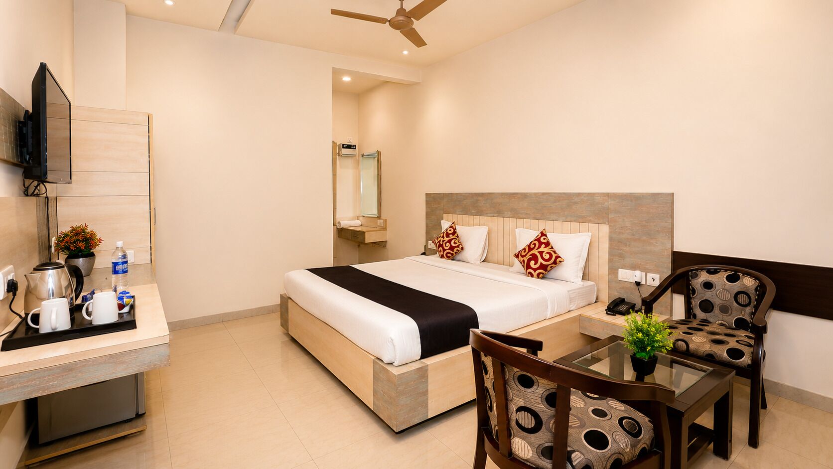 Habitación de hotel con cama, mesita de noche, silla y televisor montado en la pared.