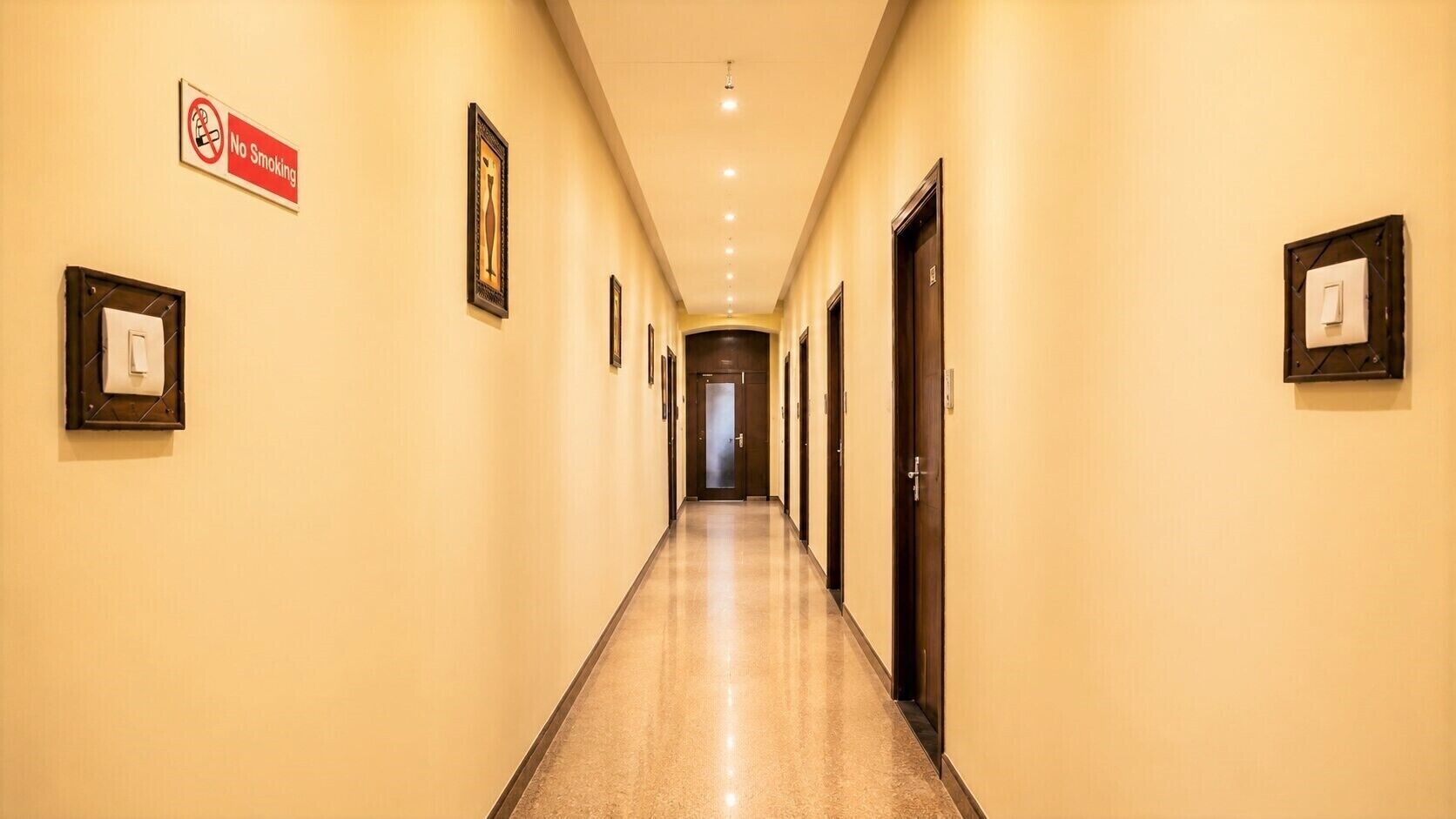 A hotel hallway with a 'No Smoking' sign, framed pictures, and doors.