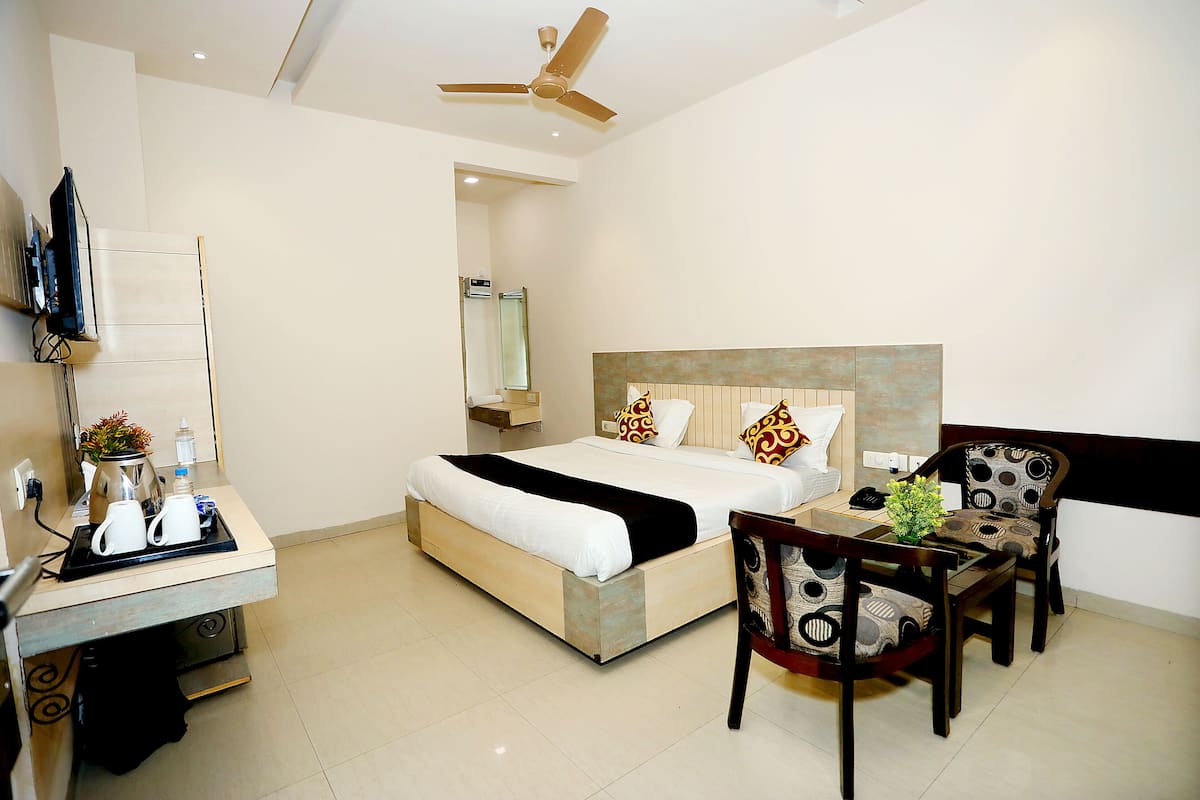 A hotel room with a bed, a desk with a computer and a telephone, a chair, and a ceiling fan.