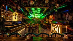 A bar with a green-lit chandelier, bar stools, and a patterned floor. - Hotel Bhagyaraj Palace - Best Hotel In Kanpur (Kanpur)