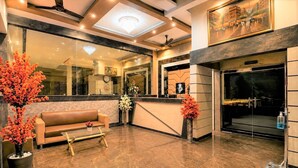 A hotel lobby with a reception desk, a sofa, a clock, and a chandelier. - Hotel Bhagyaraj Palace - Best Hotel In Kanpur (Kanpur)