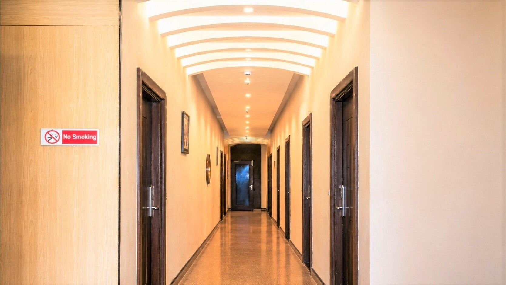 A hotel hallway with a 'No Smoking' sign, doors, and a lighted ceiling.