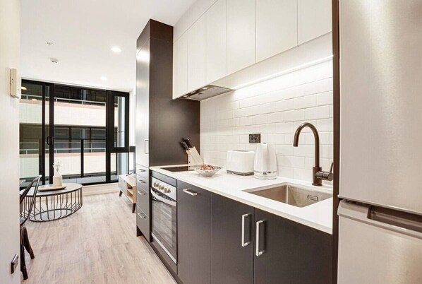 A modern kitchen with dark cabinets, a white countertop, and stainless steel appliances.