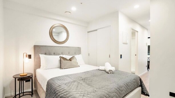 A modern bedroom with a bed, bedside table, and a mirror. - Full amenities 1-bedroom studio in CBD with pool (Auckland)