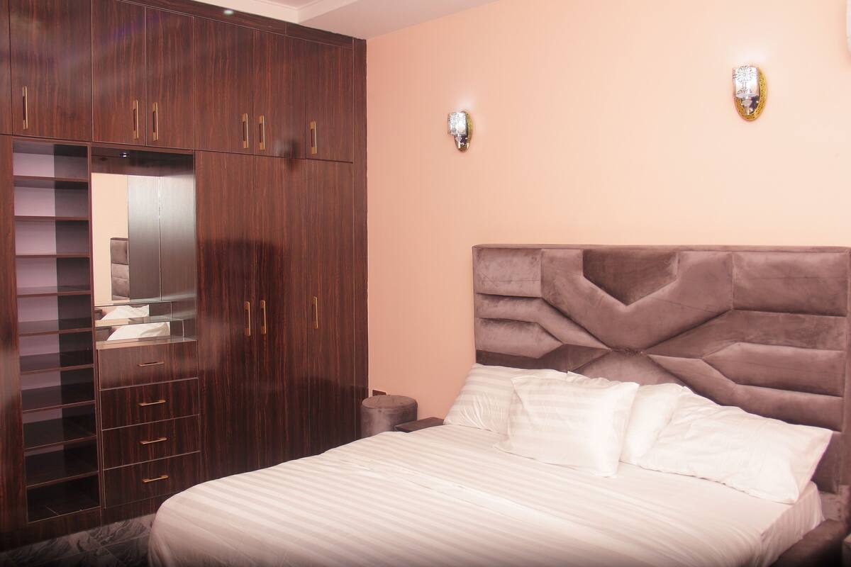 A bedroom with a large bed, a wardrobe with multiple drawers, and two wall sconces.