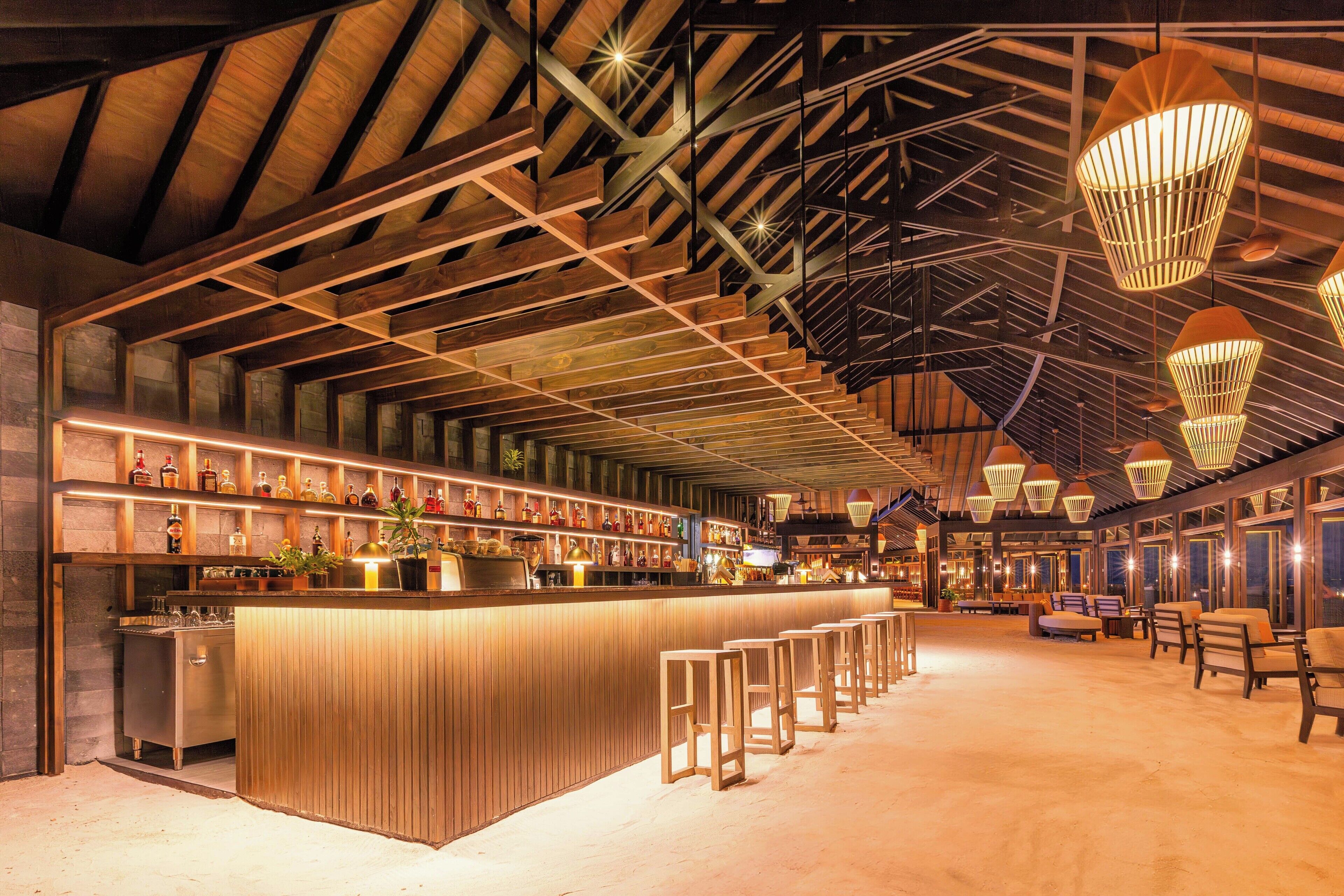 A spacious bar area with a long counter, multiple seating options, and a high ceiling with exposed beams.