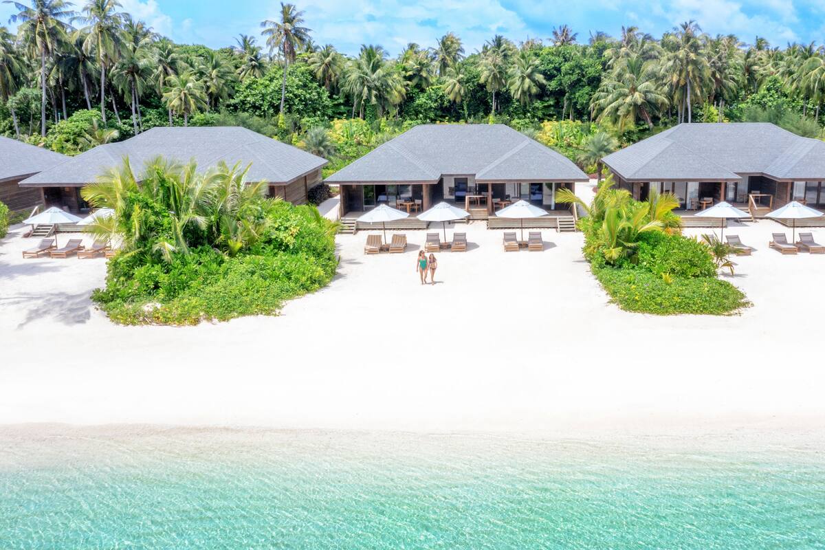 Ett lyxigt semesterresort vid stranden med flera bungalows som är byggda på pålar över vattnet. Varje bungalow har en egen pool och solstolar.