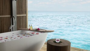 Una bañera llena de agua y flores, un muelle de madera y vistas al mar.
