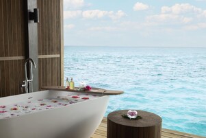 Una bañera llena de agua y flores, un muelle de madera y vistas al mar.