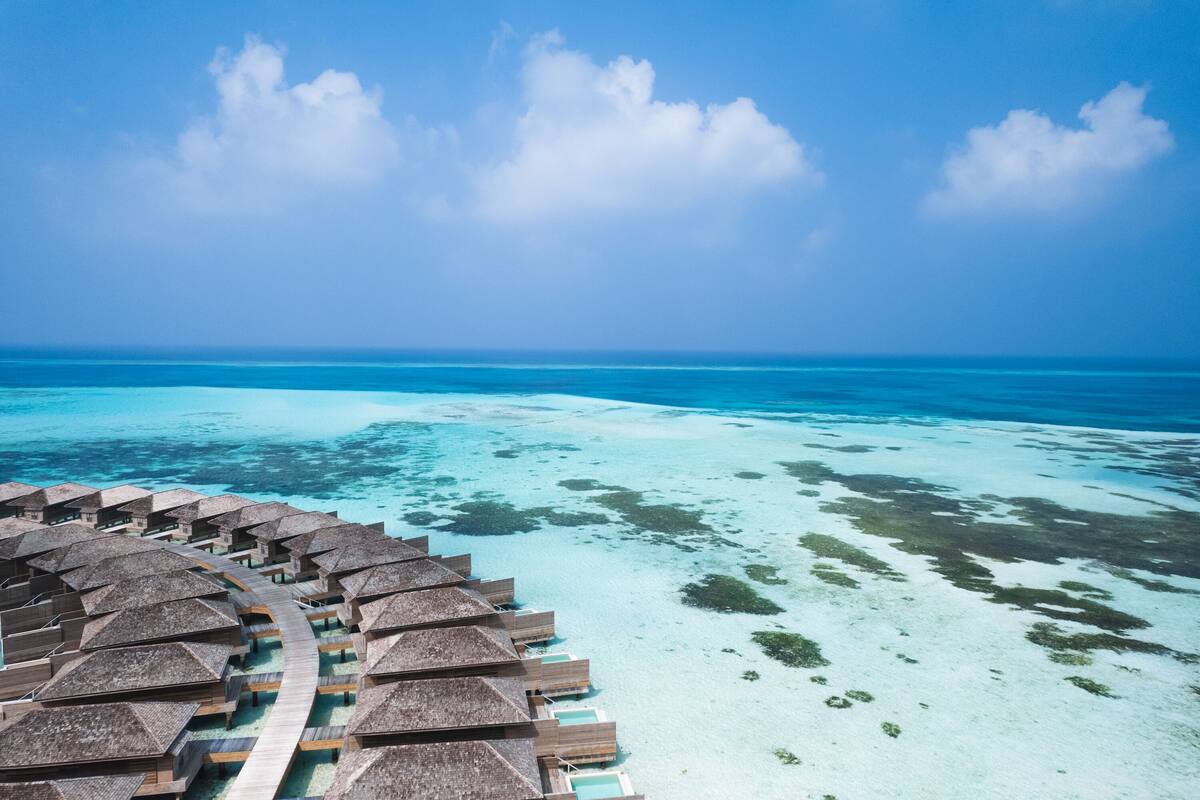 Ett flygbildsbild som visar bungalows som är byggda över vattnet, med en tydlig utsikt över det turkosfärgade havet och himlen.