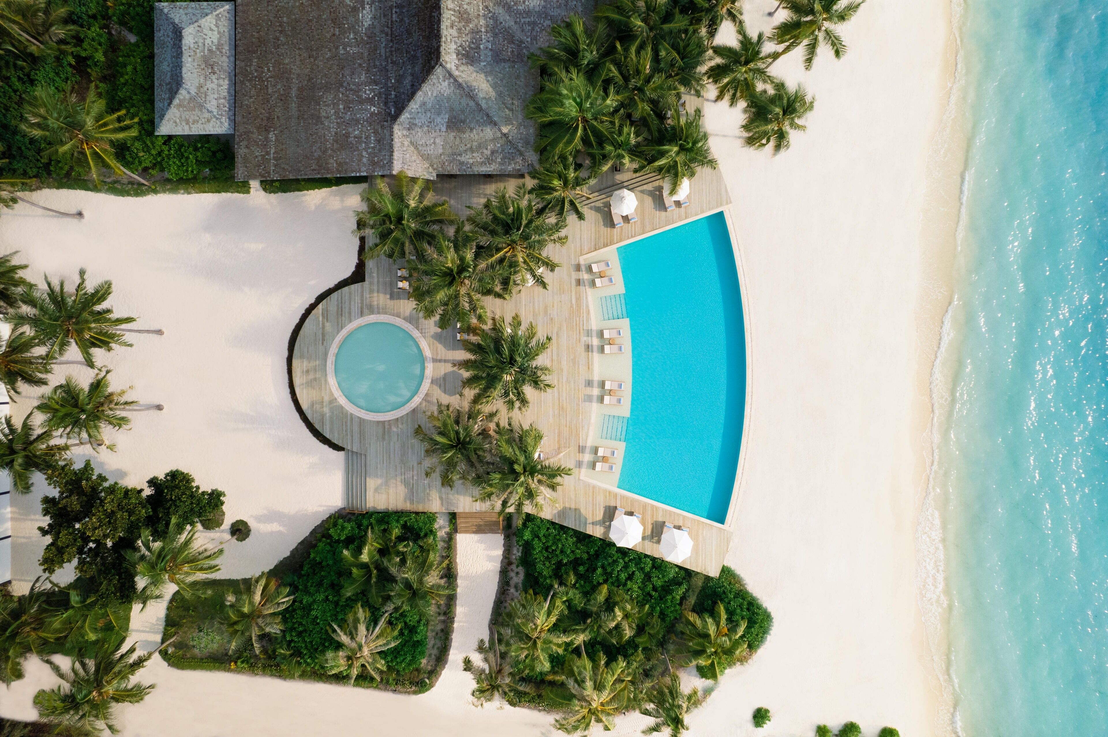 Vue aérienne d’un complexe hôtelier avec une piscine, des palmiers et une plage.