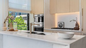 Une cuisine moderne dotée d’un plan de travail en marbre, d’appareils électroménagers en acier inoxydable et offrant une vue sur la verdure environnante.