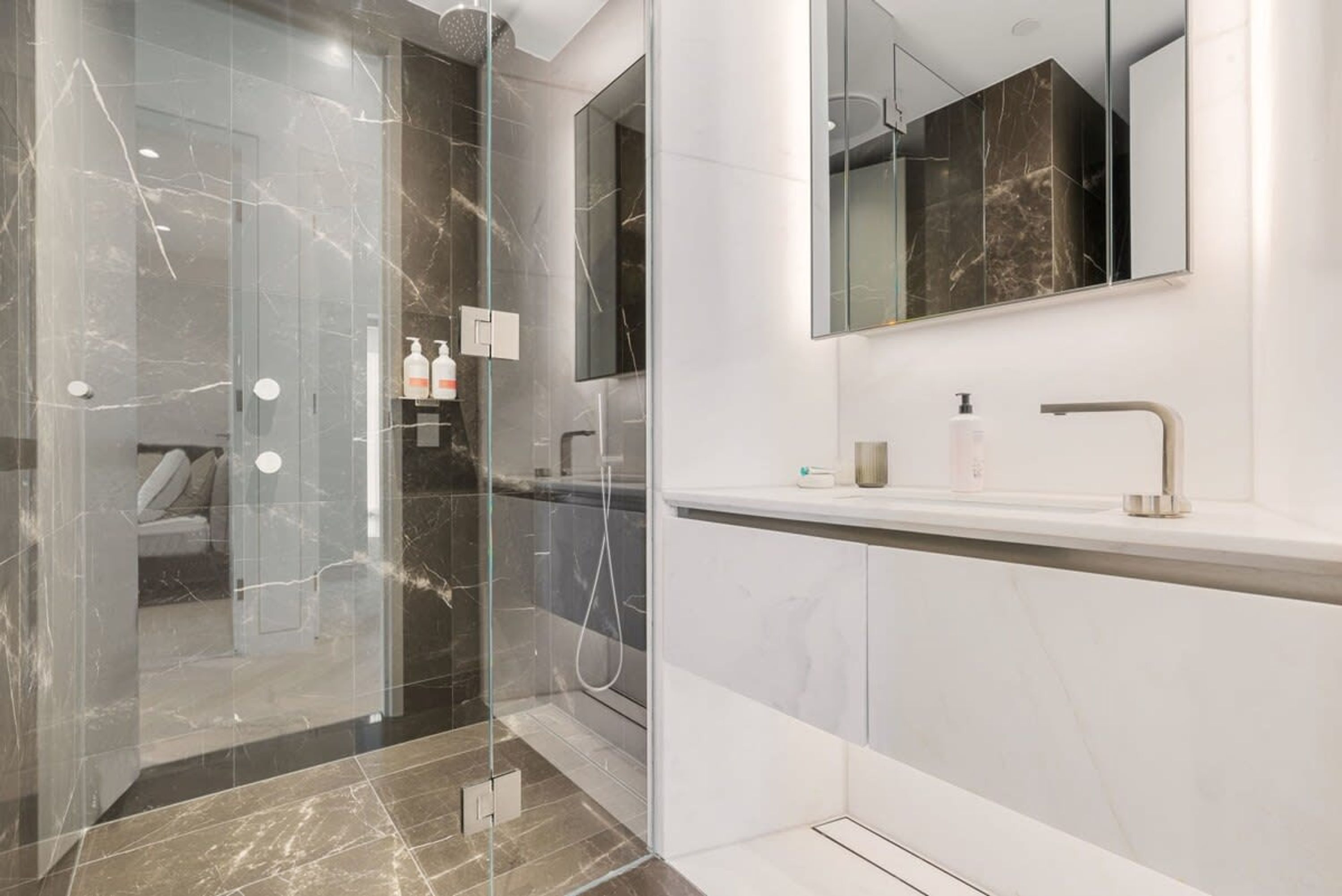 A modern bathroom with a glass-enclosed shower, a large mirror, and a white vanity with a sink and faucet.