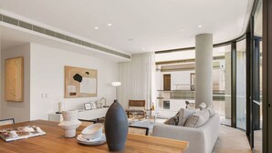 Un salon moderne avec une table à manger en bois, un canapé gris et une grande fenêtre donnant sur l’intérieur.
