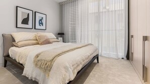 Une chambre à coucher moderne avec un grand lit, une table de chevet, une lampe et deux œuvres d’art encadrées accrochées au mur.