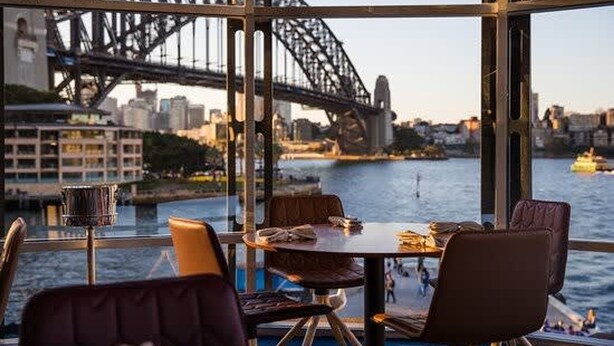 Un espace repas avec une table et des chaises, offrant une vue sur le pont du port de Sydney et sur l’Opéra de Sydney en arrière-plan.
