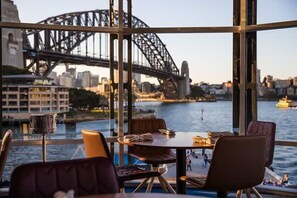 Ein Essbereich mit Tisch und Stühlen, Blick auf die Sydney Harbour Bridge und das Opernhaus von Sydney im Hintergrund.