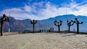 A cobblestone plaza with benches and a gate labeled "CAMPO" in the background, overlooking a body of water and mountains. - Piazza Campidoglio 3 (Tremezzina)