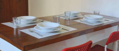 Una mesa de comedor dispuesta con platos blancos, vasos y cubiertos, acompañada de sillas rojas.
