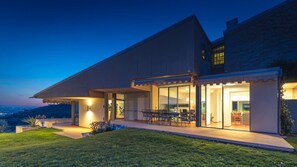 A modern house with a large patio, a dining area, and a view of the city at dusk.