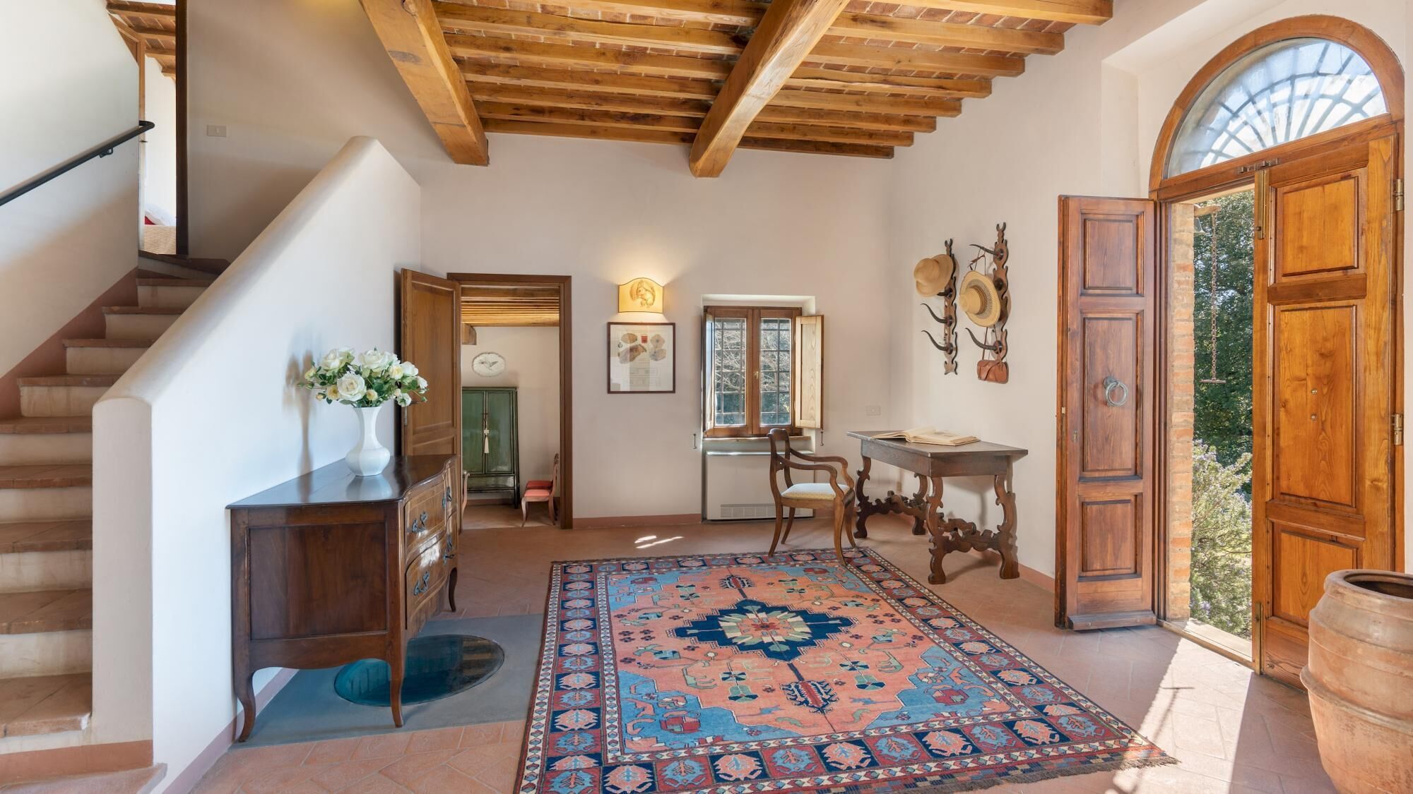 Un hall d’entrée spacieux avec un escalier en bois, un grand tapis et une porte en bois rustique.
