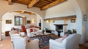 A cozy living room with white sofas, a fireplace, and a large window. - Cosciano 12 Emma Villas (Pomarance)