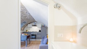 A modern kitchen with a stone arch, a dining area with a table and chairs, and a cozy living space with a sofa and a lit candle. - Pozzo Vertical Apartment With Garden and Parking (Torno)