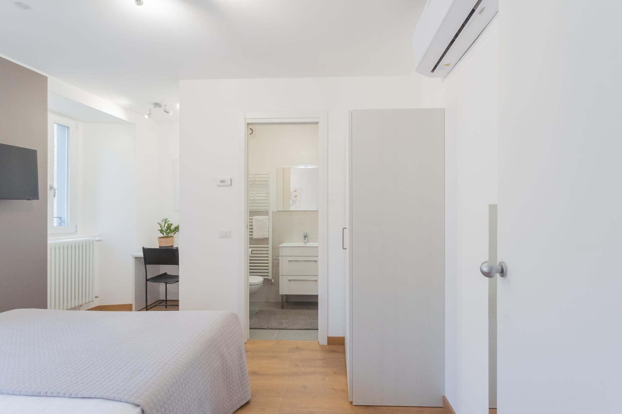 A bedroom with a bed, a desk, and a potted plant.