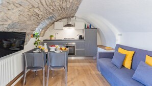 A compact living space with a stone archway leading to a kitchen, a dining area with chairs, and a sofa with cushions. - Pozzo Vertical Apartment With Garden and Parking (Torno)