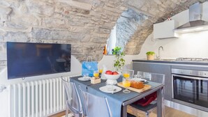 A modern kitchen with a stone ceiling, a flat-screen TV, and a dining area with a table set for two. - Pozzo Vertical Apartment With Garden and Parking (Torno)